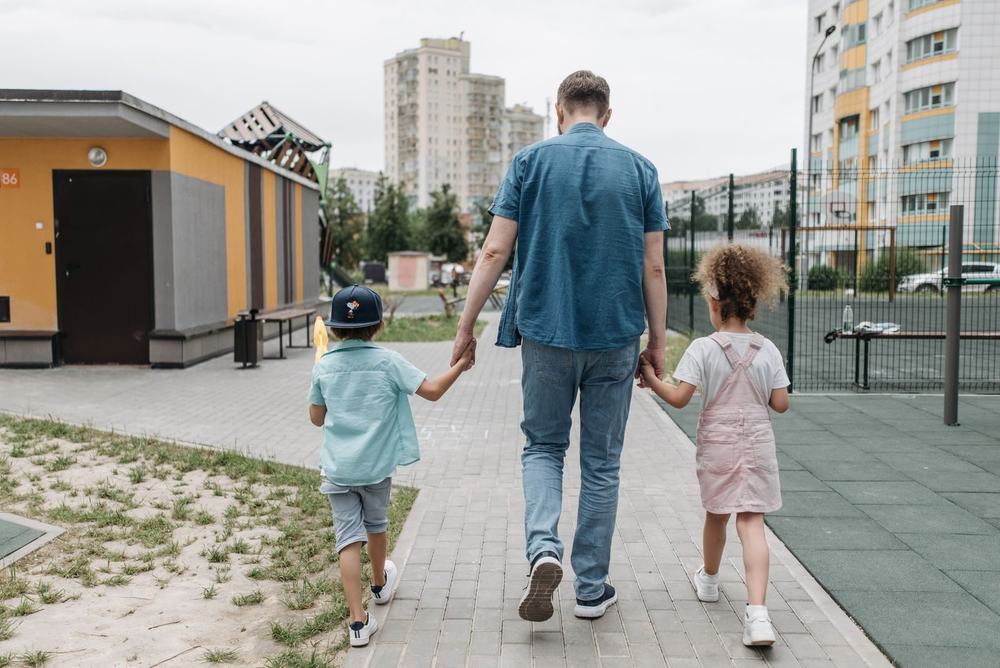 Tata z dziećmi idzie za rękę do placu zabaw, widok od tyłu